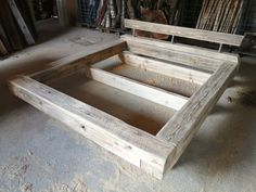 a wooden bed frame sitting on top of a floor next to a pile of clothes