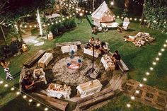 people sitting around a fire pit in the middle of a yard with lights on it