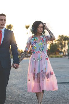 a man in a suit and tie walking with a woman wearing a pink tulle dress