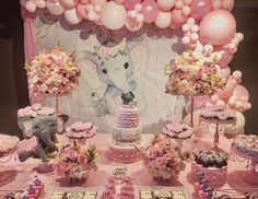 a table topped with lots of pink and white desserts next to an elephant backdrop