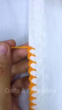 someone is stitching the edge of a piece of fabric with an orange crochet hook