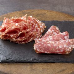 two slices of salami on top of a black slate board next to another piece of meat