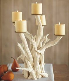 a white driftwood candle holder with five candles on it and some pears in the background