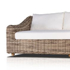 a wicker couch with white pillows on it's back and side cushions, against a white background