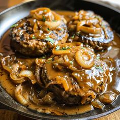 two hamburgers covered in gravy and onions on top of a skillet