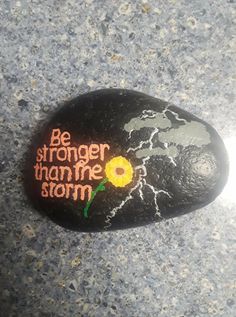 a painted rock with the words be stronger than me storm on it and a flower