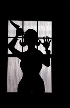 the silhouette of a woman holding a knife in front of a window