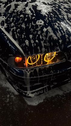 a car is covered in water with yellow letters on the hood and tail lights are visible