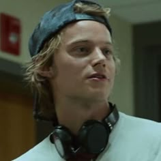 a man wearing headphones and a bandana looks off into the distance while standing in a hallway