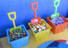 a table topped with plastic containers filled with candies and pineapples next to a blue wall