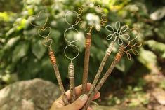 a person holding four branches with hearts on them in front of some rocks and trees