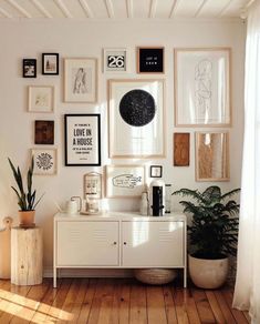 a white room with lots of framed pictures on the wall and plants in vases