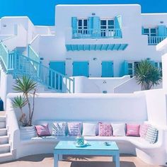 a white house with blue shutters and pink pillows on the couches in front of it