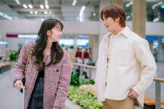 a man and woman standing next to each other in front of a planter filled with flowers