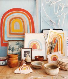 art work displayed on wooden table in front of wall with rainbow painting and other items