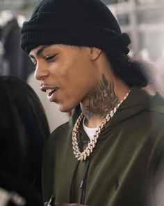 a young man with tattoos on his neck looking at his cell phone while wearing a beanie