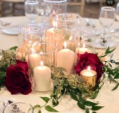 a table topped with lots of white candles and red roses on top of each other