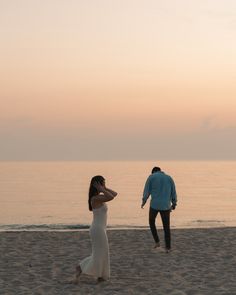 a man and woman walking on the beach at sunset