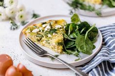 a white plate topped with a slice of quiche next to a fork and salad