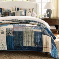 a bed with blue and white quilts on it in a bedroom next to a window