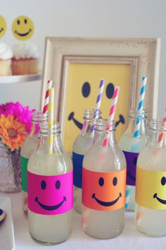 four bottles with faces painted on them are lined up in front of a cupcake