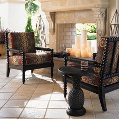 two chairs and a table in front of a fireplace with candles on the mantles