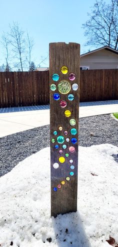 a wooden post with colorful glass buttons on it in the snow next to a fence