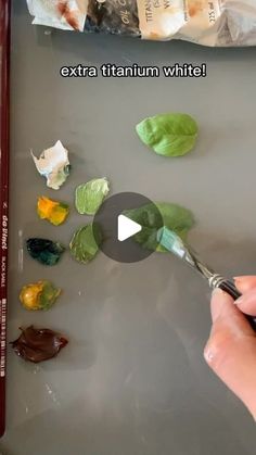 someone is painting leaves on a tray with white paint and red crayon pencils