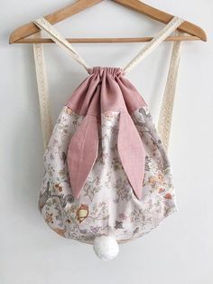 a pink and white bag hanging from a wooden hanger with a bow on it