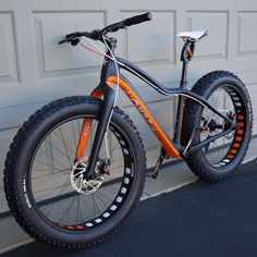 an orange and black mountain bike parked in front of a garage door on the sidewalk