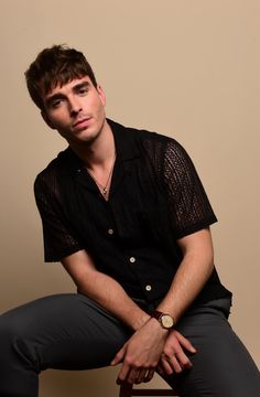 a young man sitting on top of a stool wearing a black shirt and grey pants