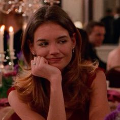 a woman sitting at a table in front of a candlelight chandelier with her hand on her chin