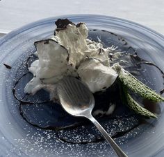 a blue plate topped with ice cream and whipped cream next to a spoon on top of it