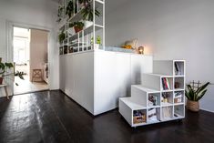 a living room filled with lots of white furniture and plants on top of bookshelves