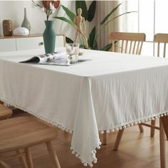 a white table cloth with pom - poms on it and two vases in the background