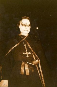 an old photo of a man dressed in black and wearing a cross on his chest