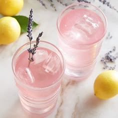 two glasses filled with pink lemonade and lavender sprigs next to lemons