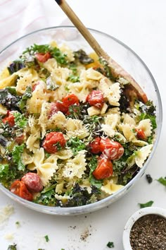 a bowl filled with pasta and vegetables next to a wooden spoon on top of a table