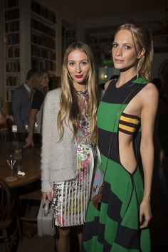 two beautiful women standing next to each other in front of a table with wine glasses