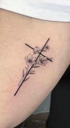 a cross with flowers on the side of her thigh is shown in this tattoo design