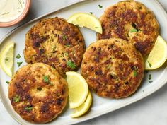 three crab cakes on a plate with lemon wedges and ranch dressing in the background