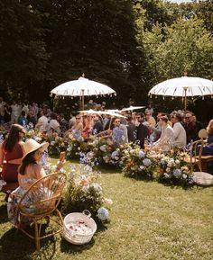 a group of people sitting on top of a lush green field next to umbrellas