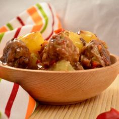 a wooden bowl filled with meatballs and pineapples on top of a table