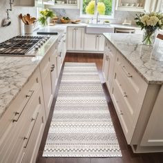 a kitchen with white cabinets and marble counter tops, along with an area rug on the floor