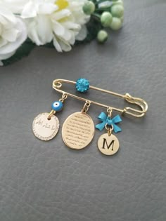 three personalized charms hang from a gold tie bar on a gray surface with flowers in the background