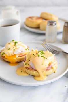 two eggs benedicts with ham and hollandaise sauce on a white plate next to a cup of coffee