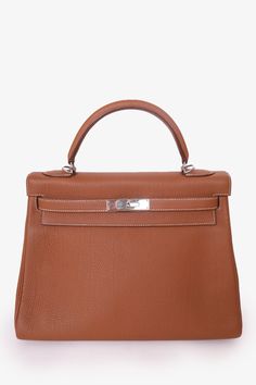 Hermés 2017 Gold Togo Retourne Kelly 32 with Strap. Top handle. Signature front Kelly closure. 3 interior wall pockets; 2 slip and 1 with zip closure. Protective metal bottom. Removable strap. Silver-tone hardware. Contrast stitching. Year: 2017Dimensions: 10.75" width x 8" height x 4.5" depth Condition: This item is in good pre-loved condition with minor signs of wear throughout. Minor scratching on hardware. Hermes Kelly 32, Cottagecore Bag, Mens Spring Shoes, Kelly 32, Pop Clothing, Wrist Stacks, Iconic Bags, Strap Top, Interior Wall