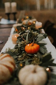 a long table with candles, pumpkins and greenery on it is set for an outdoor dinner