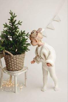 a baby in white plays with a small christmas tree