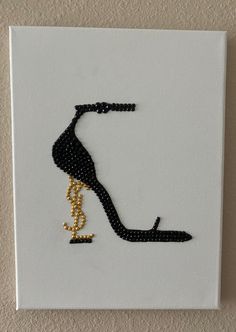 a black and gold high heeled shoe on a white canvas with pearls hanging from the side